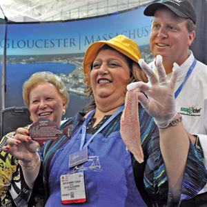From left, Angela Sanfilippo, longtime president of the Gloucester Fishermen’s Wives Association, Gloucester Mayor Sefatia Romeo Theken, and Todd Snopkowski of SnapChef – whose team helped the Fishermen’s Wives prepare vats of their famous redfish soup served at Seafood Expo in Boston. Several Gloucester seafood companies donated the 125 pounds of redfish that went into the soup. Romeo Theken displays one redfish. Susan Pollack photos